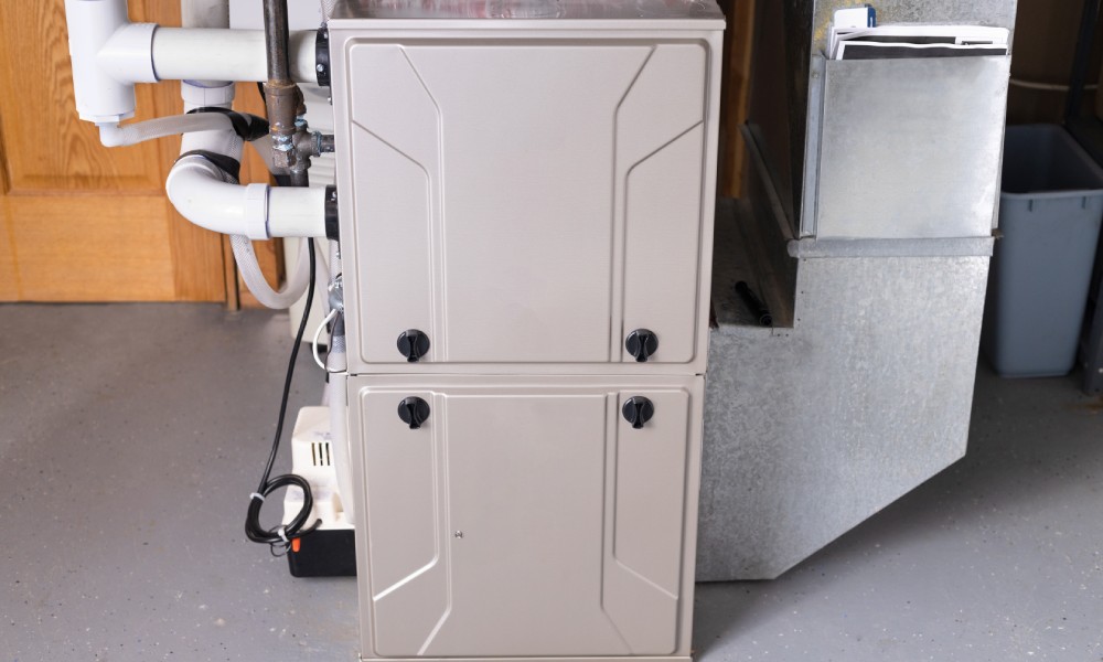 A light grey double-stage high-efficiency gas furnace standing on concrete floor in a residential basement.
