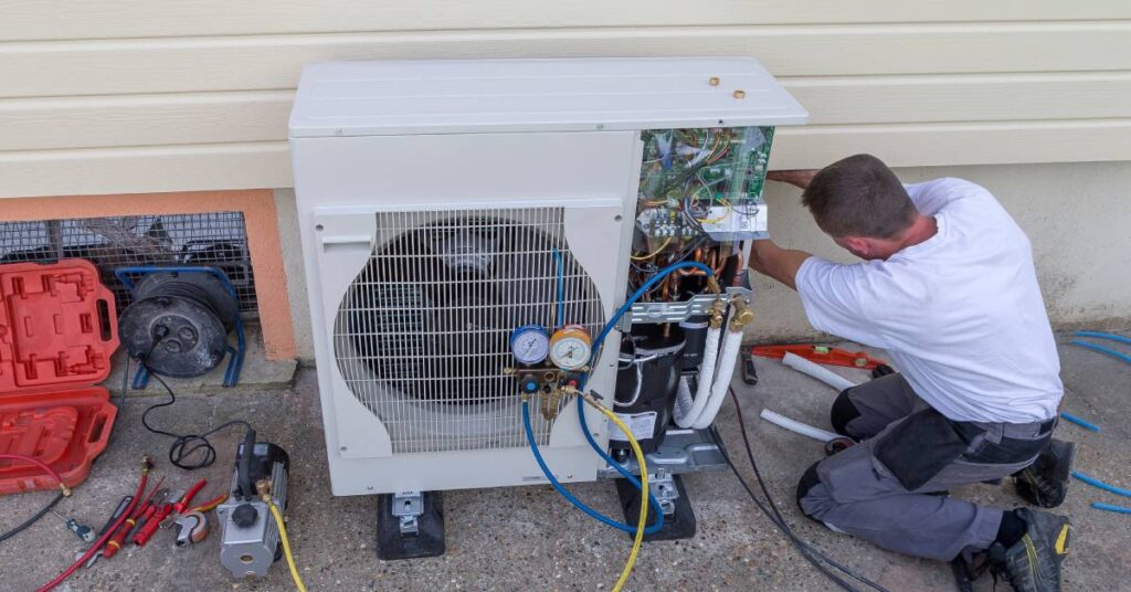 A man works on the installation of a heat pump using various tools to measure and wire the unit outside someone's home.