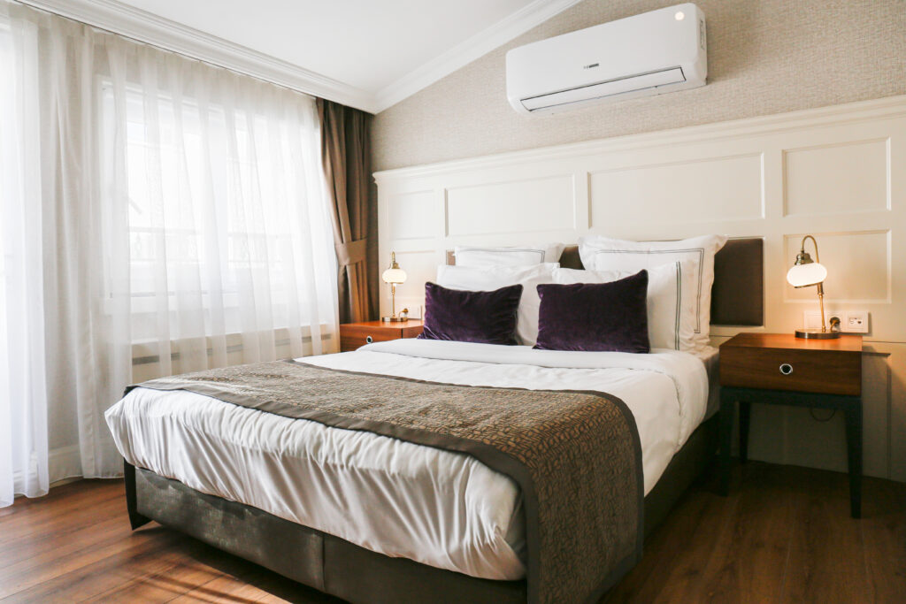 A bedroom with a queen-sized bed adorned with brown and white pillows and blankets. A ductless air conditioner hangs over it.