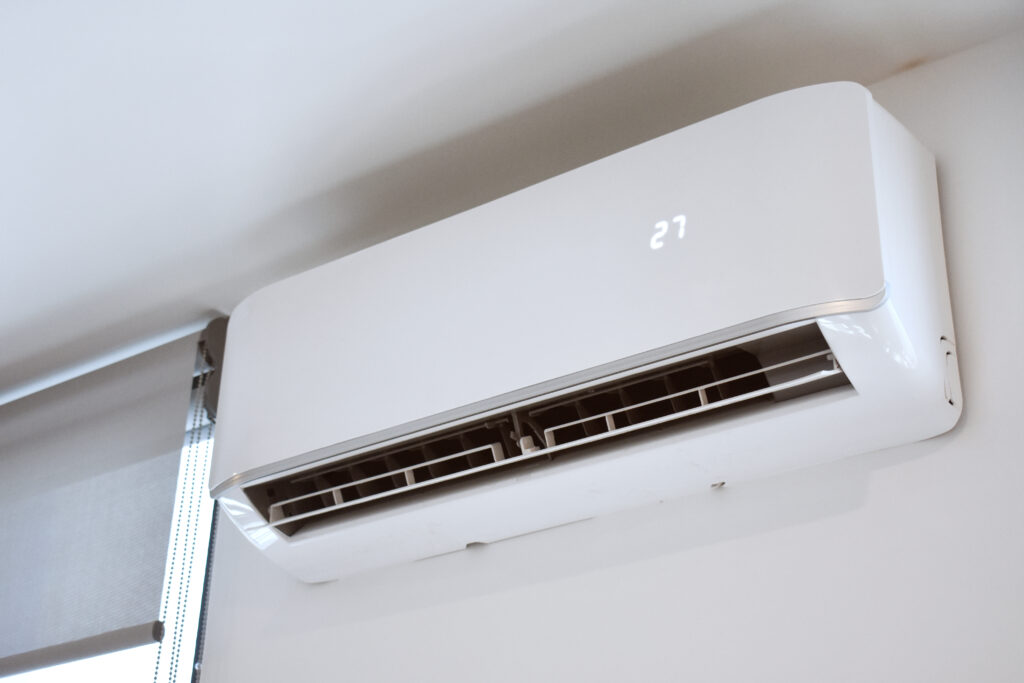 A ductless air-conditioning unit installed on the white wall of a room with a glowing "27" on its surface.