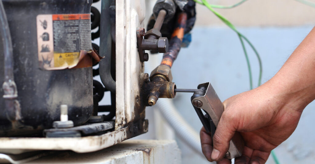 A rusty furnace with layers of dirt and peeling metal being worked on by a person turning a set of hex wrenches on a screw.