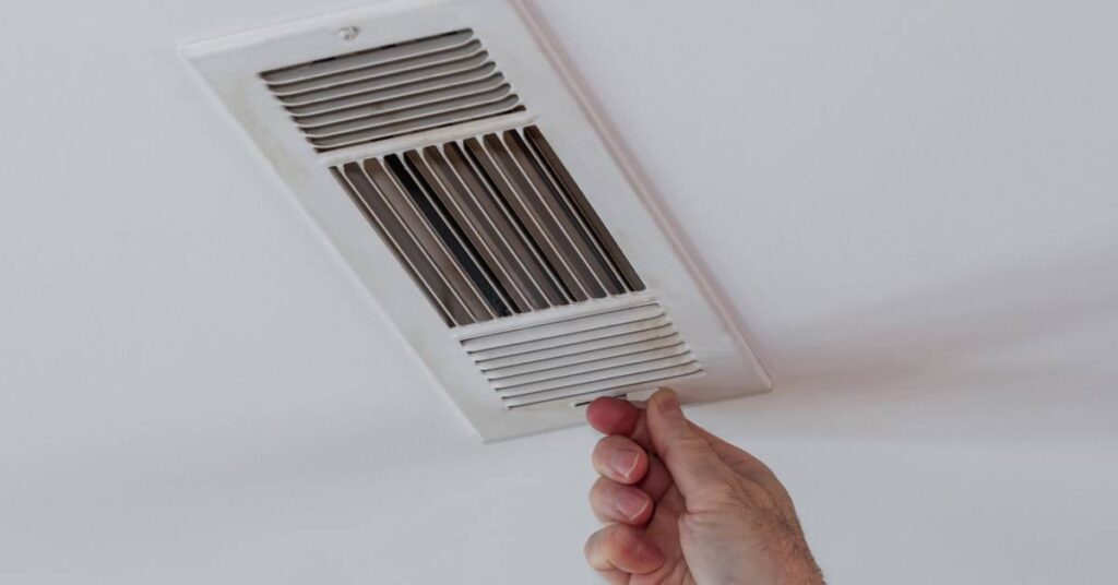 A person grabs the switch on the side of a vent installed in a white ceiling that opens the slats.