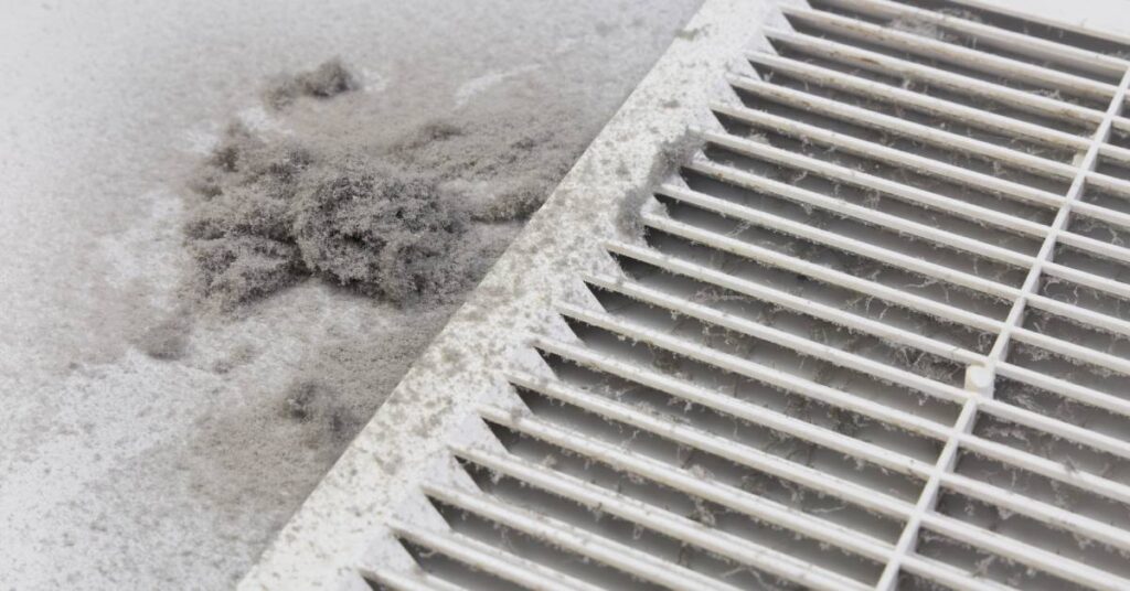 The side of a white vent with a large layer of dust clogging the openings and coating the sides with thick clumps.